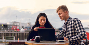 Man and woman drinking coffee and looking at laptop outdoors