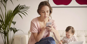 Parent using mobile with baby sitting beside them on the couch