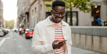 Man walking down the street smiling looking at his mobile phone.