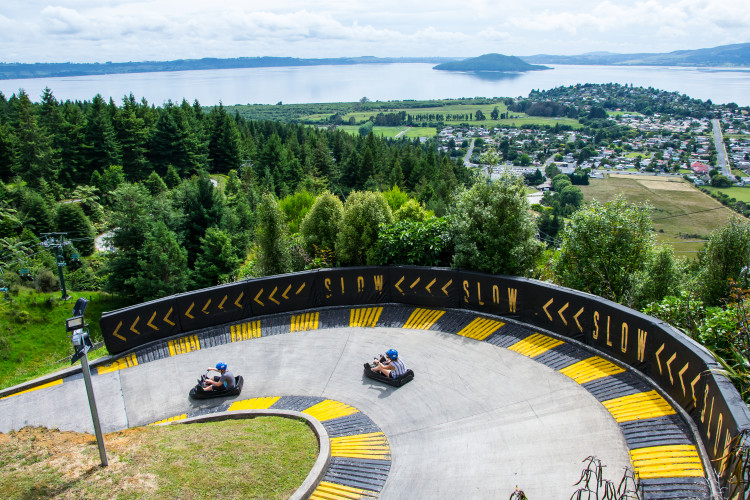 Two people going down Rotorua's luge track with the lake in the distance